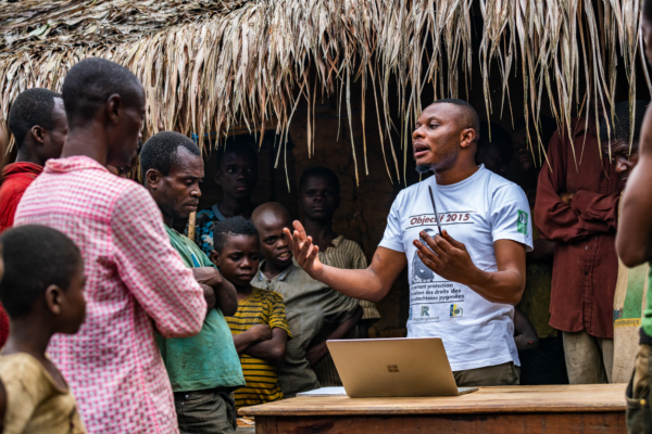 person talking to a group of people with a computer Infront of him and a object in his hand