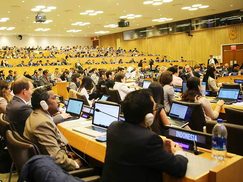 A room full of people with laptops, microphones and headphones at the UN talks
