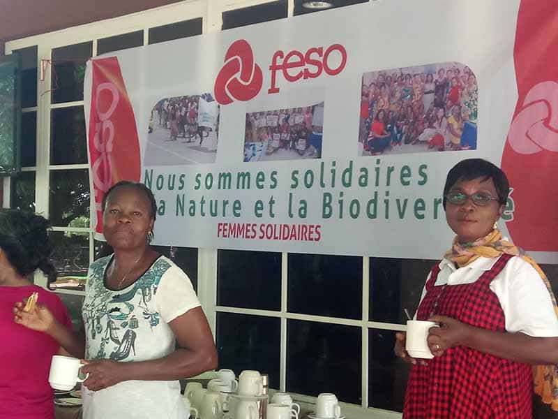 Women holding mugs in front of a banner that reads 'Nous sommes solidaures la Nature et la Biodiversity'