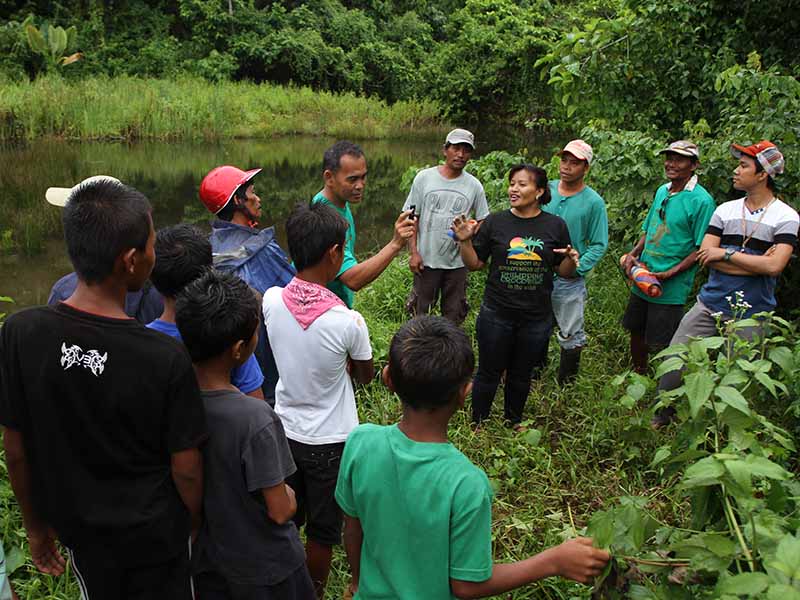 Tess Gatan-Balbas gives a speech to a group of people by the river