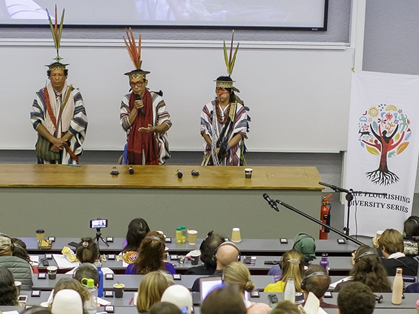 three people wearing feathered headresses talking to an audience