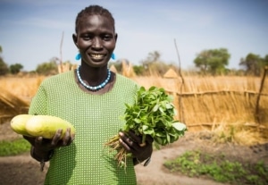 Someone in a green shirt holding up vegetables in a garden