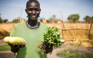 Someone in a green shirt holding up vegetables in a garden