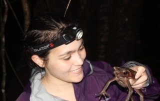pria smiling holding a frog in her hand in the dark with a headtorch