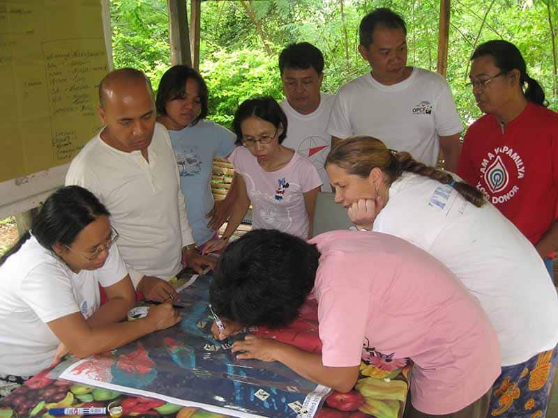 A group of people standing around a table looking at a poster someone is writing on