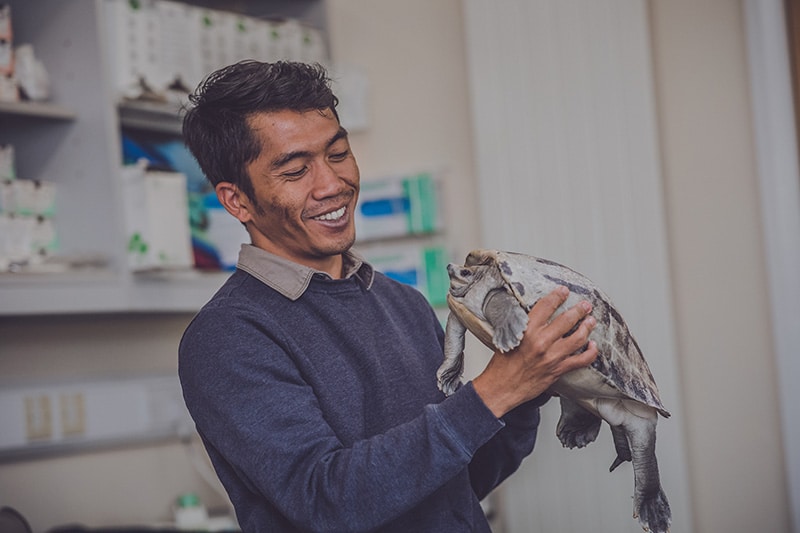 A man holds a large terrapin in his hands in a laboratory with a wide smile.