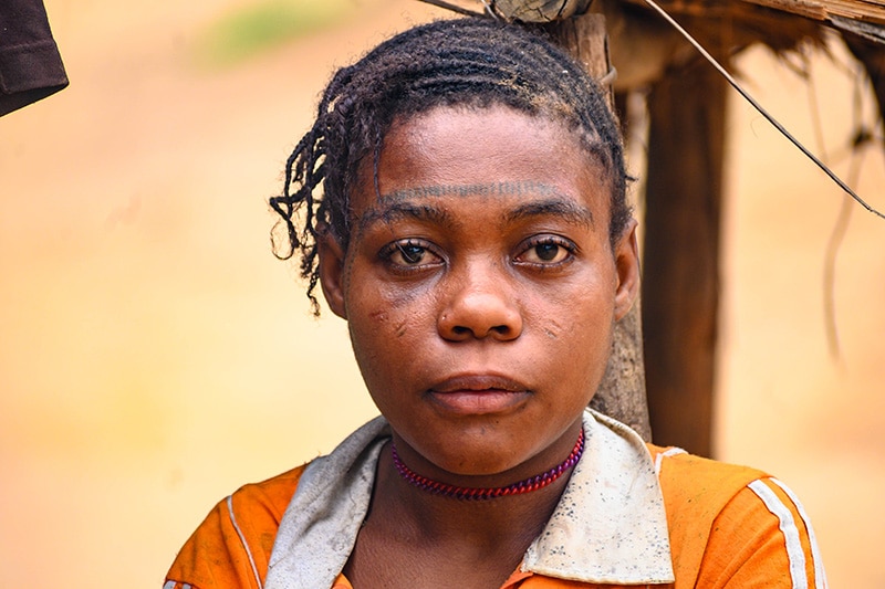 A woman stares into the camera leaning against a wooden pole