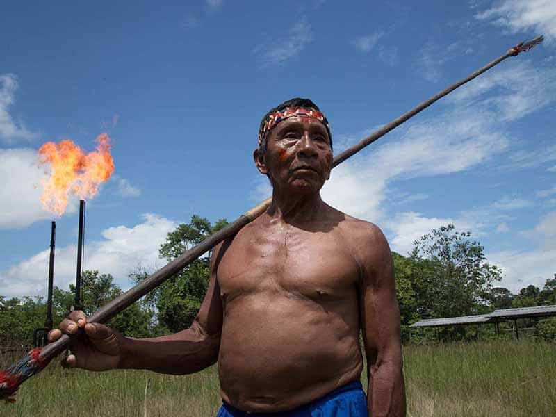 Oil flares light up behind Indigenous Waorani holding spear