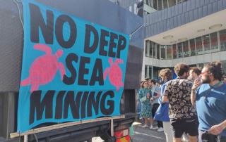 A banner reading 'No deep sea mining' outside a building with a crowd