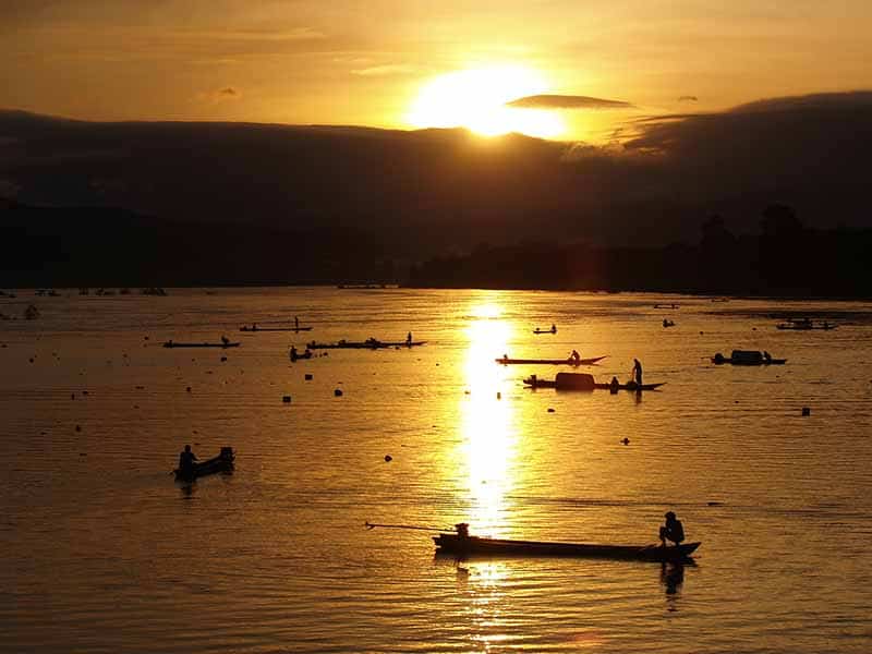 A scene of a lake at sunset with fishermen in their small boats