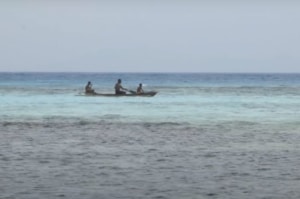 A small fishing boat with three figures in shallow coastal water