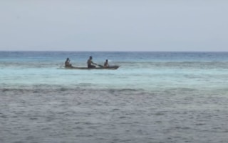 A small fishing boat with three figures in shallow coastal water