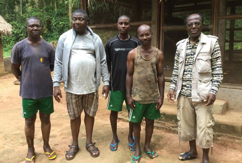 Five men in a village with a forest behind