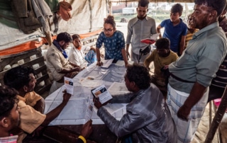 fishermen and a alifa haque stood around a map in the centre of the table.