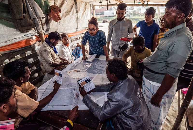 fishermen and a alifa haque stood around a map in the centre of the table.