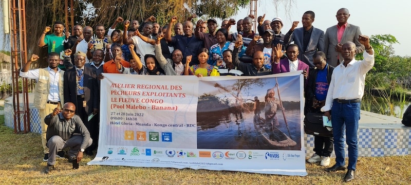 A group of people cheering while holding up a banner labelled: Atelier Regional des Pêcheurs Exploitants Le Fleuve Congo