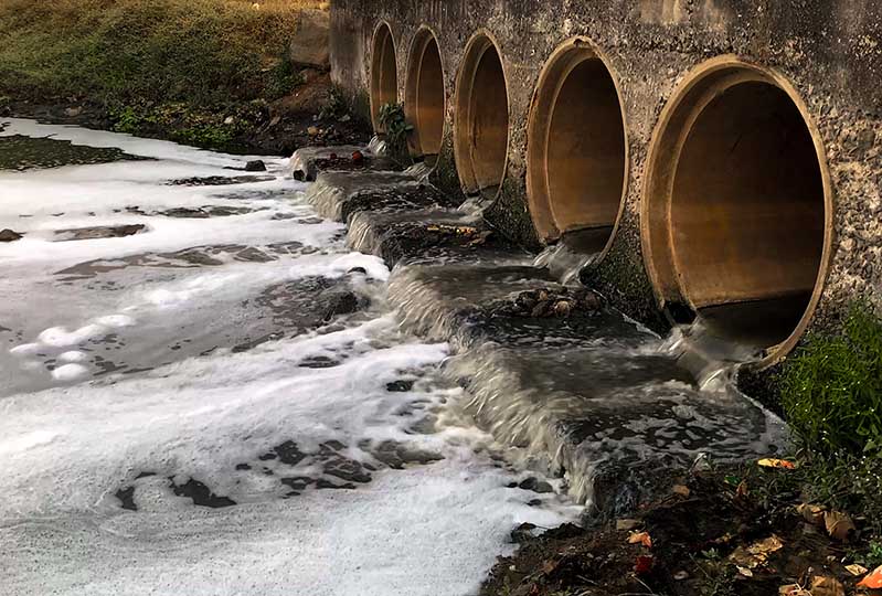 Five large discharge tunnels with murky effluent flowing into a river