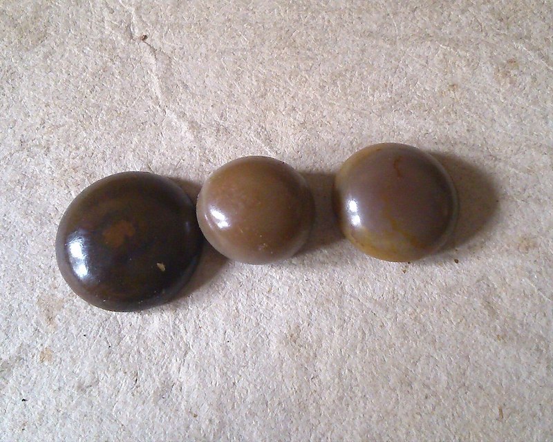 Three smooth, round, shiny stones on a grey background. The stones are various shades of dull brown.