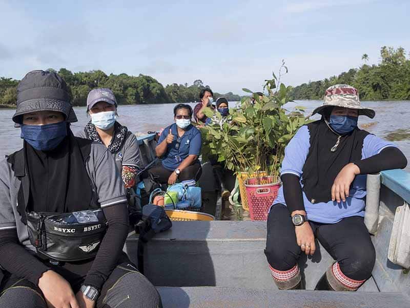Members of Synchronicity Earth partner HUTAN's restoration team on a boat on a river in Malaysian Borneo en route to plant tree seedlings