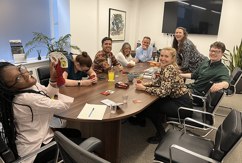 Group of people smiling around a boardroom table with boardgames and cards