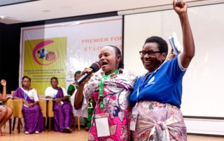 Marie Dorothée Lisenga Bafalikike (left), an Indigenous Baaka woman from Yahuma territory in the DRC chants in solidarity with another forum participant, who has a triumphant fist raised in the air