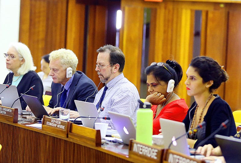 People sit with laptops and headsets at a policy meeting. 