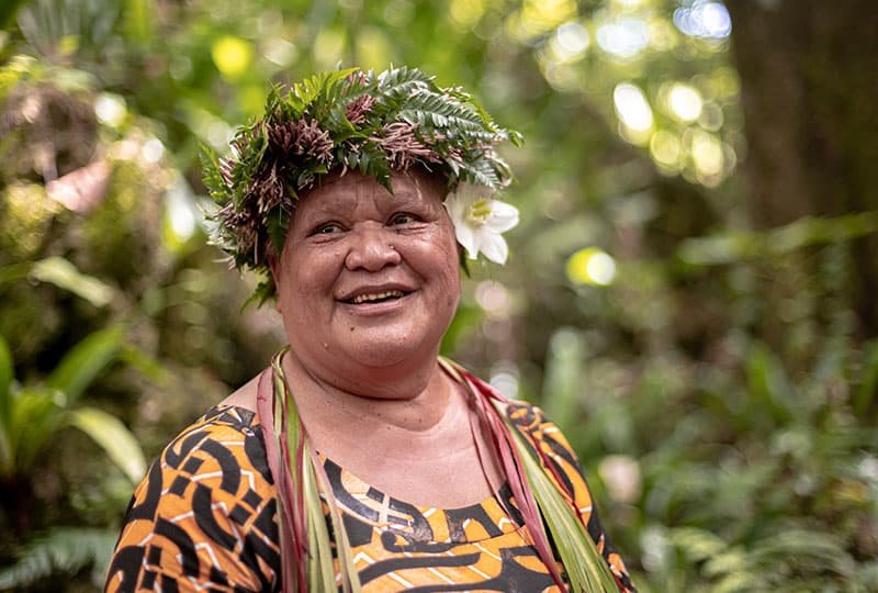 An Indigenous Cook Islands woman with a headdress made of leaves on a forest background.