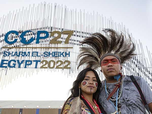 Two Terena Indigenous Youth stand underneath sign for COP27 in Sharm el Sheikh