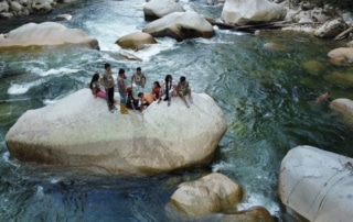 A group of people sitting on a rock in a river.