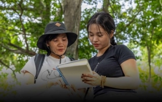 Two female members of WildAct stand in forest looking together at a book