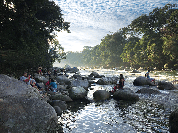 Young people sitting on large boulders in the middle of a beautiful river in the forest