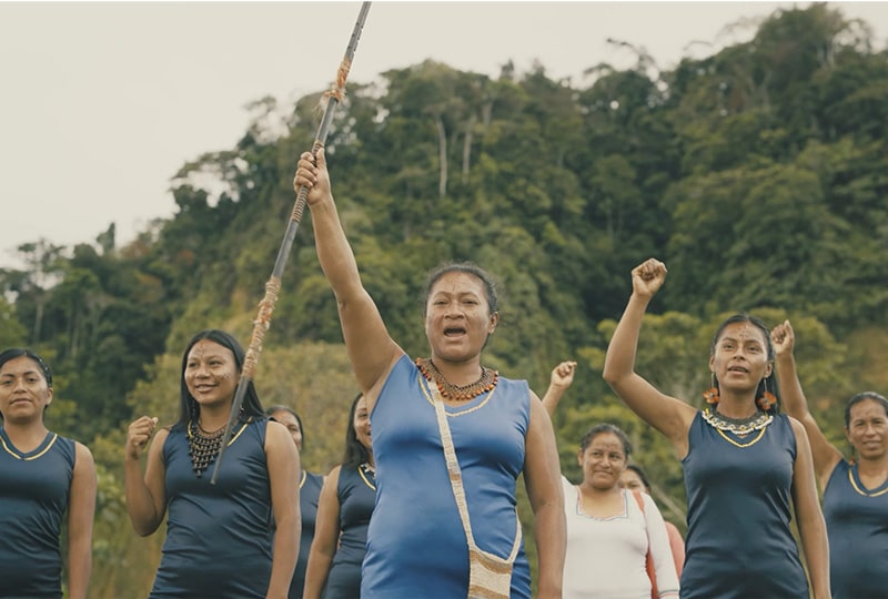 six women stand firmly with their hands extended in the air