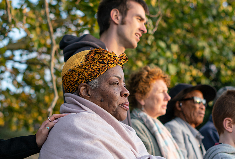 A woman in a headscarf sitting down alongside two other people looks into the distance with a man standing behind them