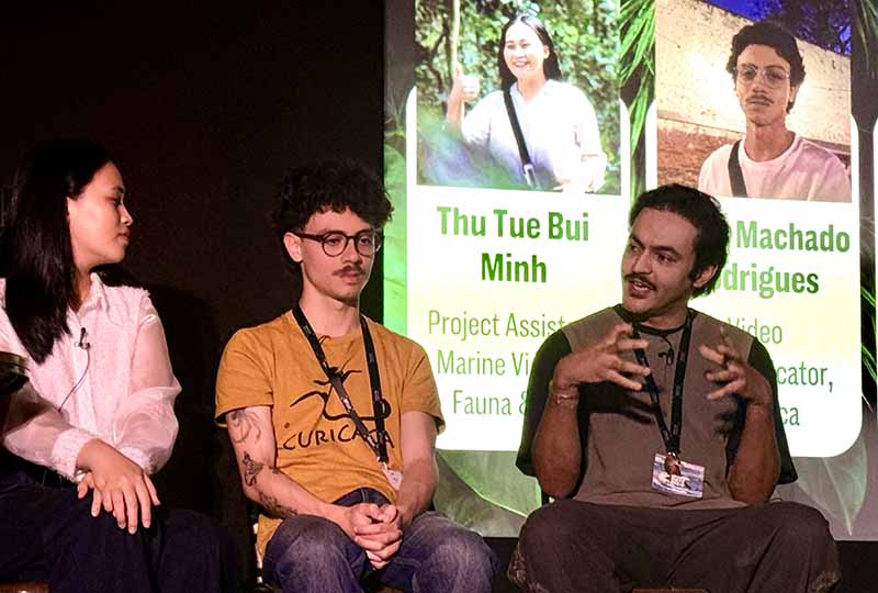 Three people - two men and one woman - sitting on stage talking