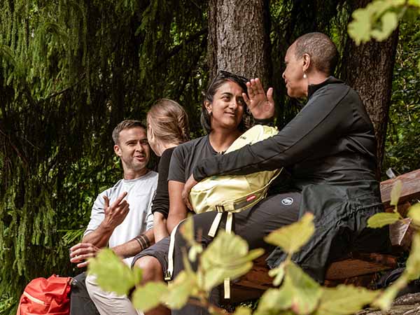 Four people in two pairs deep in conversation in a wooded alpine setting