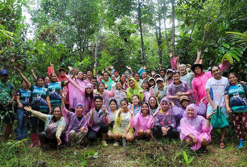 Image of a group of youth and community leaders in the rainforest. They are wearing variously coloured rain ponchos and smiling at the camera.