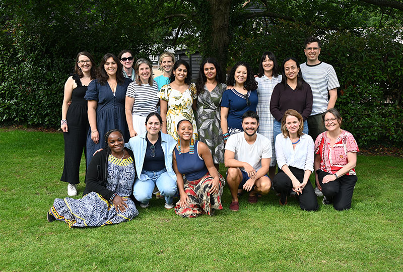 Group photo of the Synchronicity Earth Programmes team. Two rows of people, on squatting or sitting in front and one standing on a lawn in front of trees.