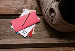 Image from above of a bench with a person sitting beside a stack of letters.