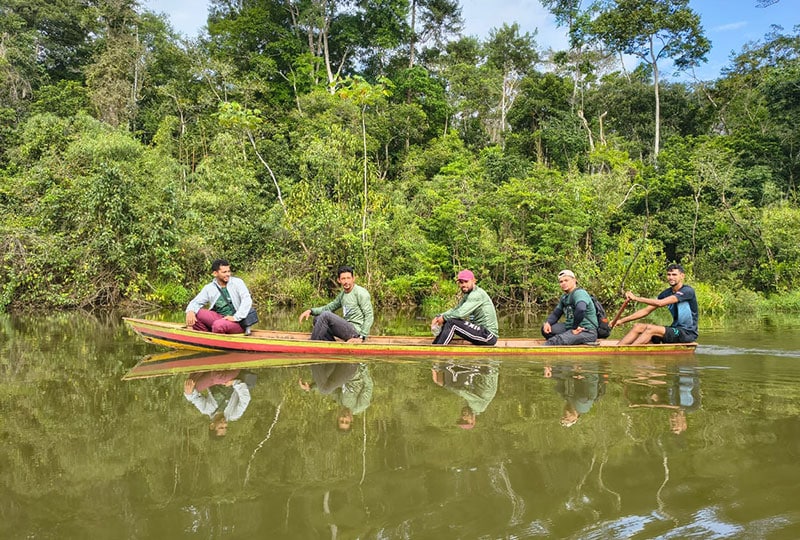5 men sit in a small boat, crossing the Juruá river.